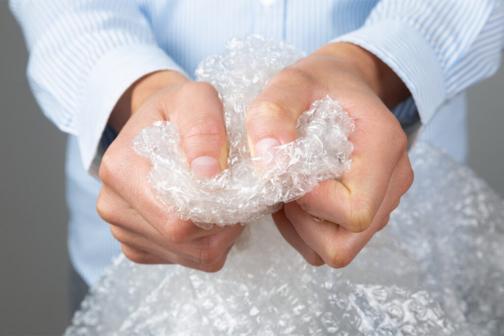 A person in a blue striped shirt is squeezing and popping clear bubble wrap with both hands.