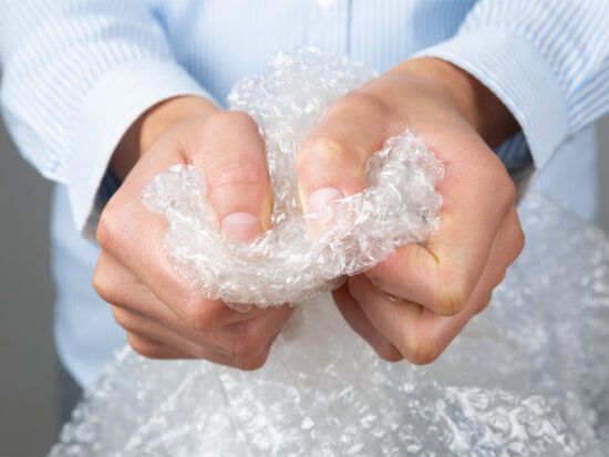 A person in a blue striped shirt is squeezing and popping clear bubble wrap with both hands.