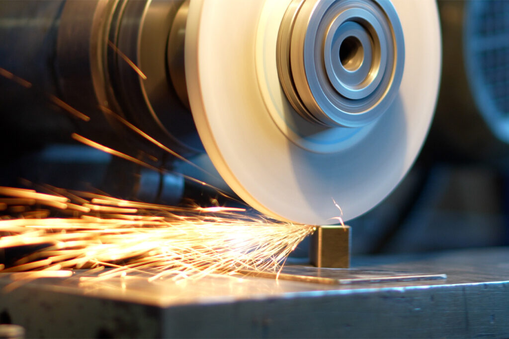 A grinding wheel sharpens a metal piece, producing bright orange sparks that fly in various directions on a workbench.