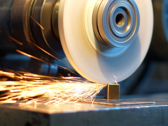 A grinding wheel sharpens a metal piece, producing bright orange sparks that fly in various directions on a workbench.